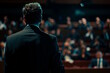 © MarGa - Young white man presenting to an audience in a dark conference room. Concept for public speaking and business presentation