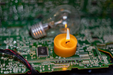 Wall Mural - A burning candle against the background of an incandescent lamp and electronic circuit boards. Blackout due to the war in Ukraine