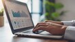 © buraratn - Businessman's hand typing on a laptop with financial charts on the screen