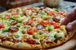 © ylivdesign - Closeup of a hand taking a piece of colorful vegetable and pepperoni pizza