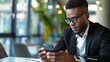 © Falk - Side view portrait of African-American businessman sitting at table and using smartphone