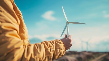 A detailed view of hands holding a wind turbine model against a backdrop of clear skies, symbolizing the conservation effort and the power of renewable energy in our hands.