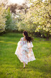 © Michael Rekochinsky - Full-length portrait of a beautiful brunette caucasian woman running in blossoming apple garden in white floral dress on a fresh green grass shot from her back with her hair flying