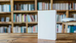 © Gita - A blank book standing upright on a wooden table with a blurred bookshelf background, ideal for cover design presentations and marketing.  mockup