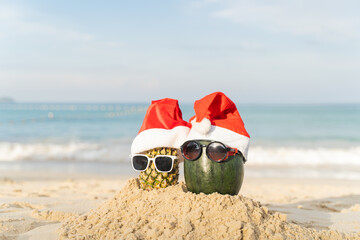 Santa Claus pineapple and watermelon couple wearing stylish sunglasses on the sand contrasting with the sea. wearing a christmas hat Christmas and New Year holiday ideas on the beach, Patong, Phuket