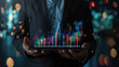 © sommersby - A businessman is shown holding a tablet with colorful financial data charts projected from it. The image is set against a blurred background of city lights at night