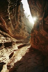 Wall Mural - A narrow canyon with a sun shining through the rocks. The sun is casting a warm glow on the rocks and the ground