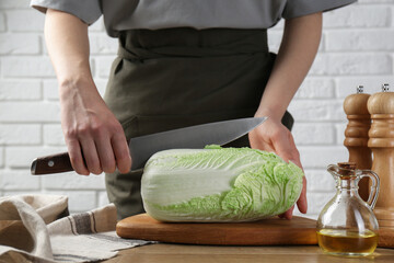Woman cutting fresh Chinese cabbage at wooden table indoors, closeup