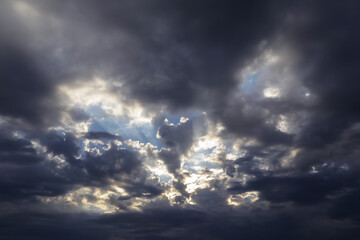 Wall Mural - Epic dramatic storm dark grey clouds against blue sky with sun and sunlight