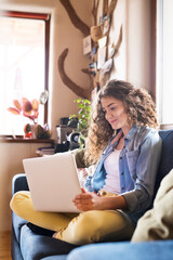 Wall Mural - A beautiful university student having online class, e-learning sitting at home on the couch, laptop on knees.