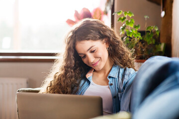 Wall Mural - A beautiful university student having online class, e-learning sitting at home on the couch, laptop on knees.