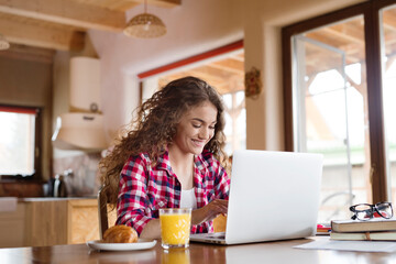 Wall Mural - A beautiful university student is writing her thesis on a laptop, sitting at home on the couch.