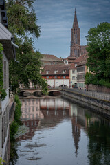 Canvas Print - Strasbourg, France - 06 28 2023: View of typical colorfull Alsatian facades buildings and Notre Dame Cathedral of Strasbourg from the Covered Bridges of Strasbourg along the Ill river .