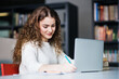 © Halfpoint - Young female student in library, focusing on final project, presentation, working on laptop. University student preparing for final exam.