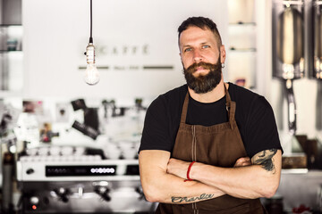 Handsome male barista working in coffee shop, standing by counter. Bartender in apron preparing coffee drink.