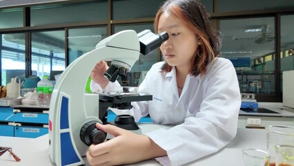 Wall Mural - cute scientist schoolgirl in lab coat looks through microscope for study microbiology in laboratory.