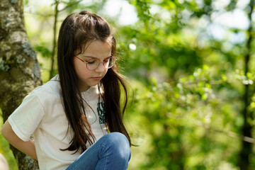 Wall Mural - Portrait of a little girl in glasses sitting on a tree branch