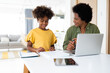 © Dorde - Smiling mother helping her elementary age daughter with her homework while she's sitting at the desk at home. Young schoolgirl and mother doing homework together. They are also using laptop.
