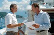 © Yuliia - Full body photo of a mature male Caucasian insurance agent discussing policy details with a boat-owner using documents on the deck of a yacht
