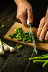 Wall Mural - A cook cuts green garlic on a cutting board with a knife to prepare a vegetarian dish. Place for advertising