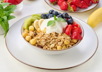 Wall Mural - Granola with strawberries, kiwi, banana and blueberries in a round plate topped with yogurt on the table.