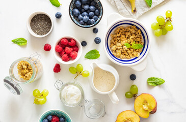 Wall Mural - Set of various ingredients for cooking a healthy breakfast setup with granola, assorted fresh fruits, chia seeds and yogurt on a white marble background top view