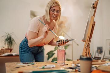 Wall Mural - Smiling artistic hipster girl mixing colors on palette at atelier.