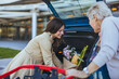© Dragana Gordic - A Caucasian adult daughter is cheerfully loading groceries into the car trunk, assisting her elderly mother outside a shopping center.