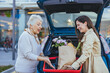 © Dragana Gordic - A cheerful Caucasian woman helps her elderly mother with grocery bags, placing them into the car trunk in a parking lot, reflecting a caring family moment.