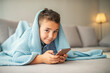 © Dragana Gordic - Photo of young boy relaxing on sofa and looking at his smart phone. Leisure, children, technology, internet communication and people concept - smiling boy with smartphone texting message