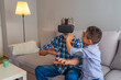 © Dragana Gordic - senior man using VR glasses sitting on sofa at home with his grandson. Exciting experience. Cheerful aged man wearing VR glasses while resting with his grandson.