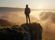© DWN Media - A man stands on the edge of a cliff, overlooking a misty valley at sunrise.
