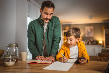 Father with book help son who copy notes from mobile phone at home