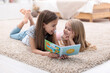 © New Africa - Cute little sisters reading book together at home