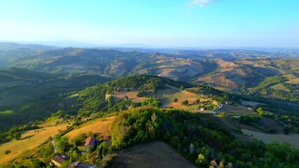 Wall Mural - Delightful aerial push-in shot from Penna San Giovanni (MC) with the vivid and sumptuous colors of the typical Marche hillscape in full display, full of thickets, perfectly manicured fields, buildings