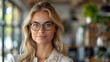 © SebuahKisah - A confident young female employee wearing glasses poses successfully for a photo in a modern office.