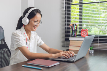 Student girl with glasses and wearing headphones watch video online webinar learn on laptop at home.