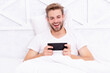 © be free - Man betting on smartphone. Video gaming online. Man watching phone. Man betting in bedroom. Video call. Millennial guy at weekend. Millennial man use smartphone in bed at home. Weekend laying in bed