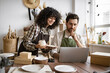 © sofiko14 - Caucasian couple of co-workers work on small pottery production business. Mature man and young curly-haired woman in aprons use laptop to take inventory of products on store website.