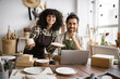 © sofiko14 - Caucasian couple of co-workers work on small pottery production business. Mature man and young curly-haired woman in aprons use laptop to take inventory of products on store website.