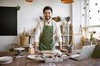 © sofiko14 - Positive male resting before making ceramic dishes from clay on background of shelves with tableware. Portrait of mature bearded male potter, standing in front of table with tools for sculpture.