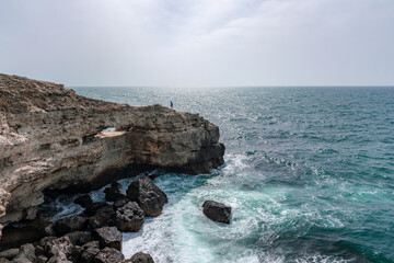 Wall Mural - A rocky cliff overlooks the ocean, with the water crashing against the rocks. The scene is serene and peaceful, with the sound of the waves providing a calming atmosphere.