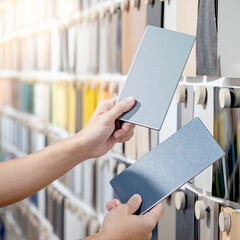Wall Mural - Designer hands compare two gray laminate sheets nearby material swatch wall display in material library. Choosing color board from collection for interior architecture and furniture finishing design