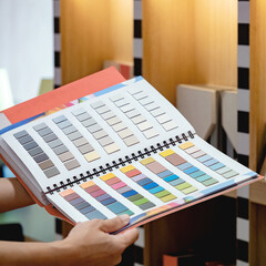 Wall Mural - Designer hand holding sample color swatch catalog in material library. Choosing finishing materials for wall and floor interior architecture or furniture design