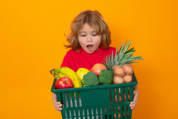 Wall Mural - Shopping grocery. Portrait of child with shopping cart full of fresh vegetables, isolated studio background. Little child in a food store. Supermarket shopping and grocery shop concept.