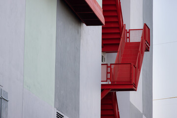 Poster - A red staircase with a white building in the background. fire escape ladder outside of building.