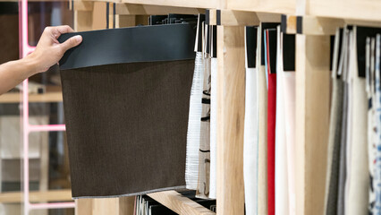 Wall Mural - Designer hand choosing dark brown fabric swatch sample for curtain or drapery design and upholstery furniture. Interior decoration material ideas.