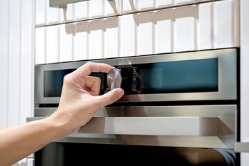 Male hand turning temperature dialing knob of oven in modern kitchen. Cooking appliance for domestic kitchen.