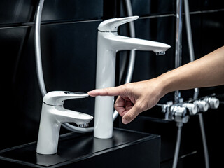 Customer hand pointing at white water faucet in home interior design showroom display. Choosing modern water tap for domestic bathroom design and decoration