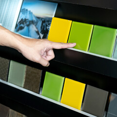 Wall Mural - Architect hand choosing and pointing at green lacquered glass tile on material samples shelf display in the material library. Colorful acrylic sheet collection for interior finishing idea